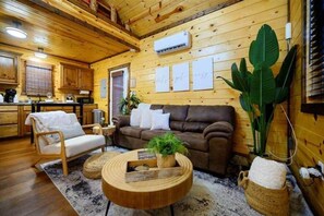 Ein gemütliches Blockhaushaus-Interieur mit Holzvertäfelung, einer Couch, einem Sessel, einem Couchtisch und einer großen Pflanze.