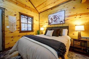 A wooden room with a bed, two bedside lamps, a window, and a wall-mounted artwork. - Beaver's Little Lodge I Couples Cabin I Romantic (Hochatown)