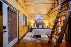 A wooden cabin bedroom with a bed, bedside lamps, a ladder, and a framed picture on the wall. - Beaver's Little Lodge I Couples Cabin I Romantic (Hochatown)