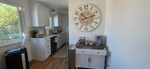A kitchen with white cabinets, a clock on the wall, and a coffee maker on the counter. - Newly Renovated Coastal Condo with Peekaboo Ocean View (San Clemente)
