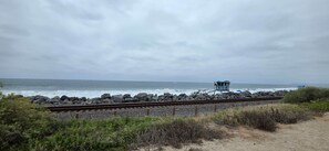 A coastal scene with a beach, rocky shoreline, and a railway track. - Newly Renovated Coastal Condo with Peekaboo Ocean View (San Clemente)