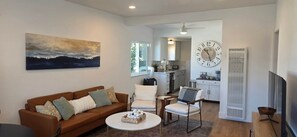 A living room with a brown sofa, a coffee table, and a painting on the wall. - Newly Renovated Coastal Condo with Peekaboo Ocean View (San Clemente)