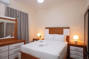 Ein Hotelzimmer mit einem Bett, zwei Nachttischen mit Lampen, einem Holz-Kopfteil, einem Spiegel und einem Fenster mit Vorhängen.