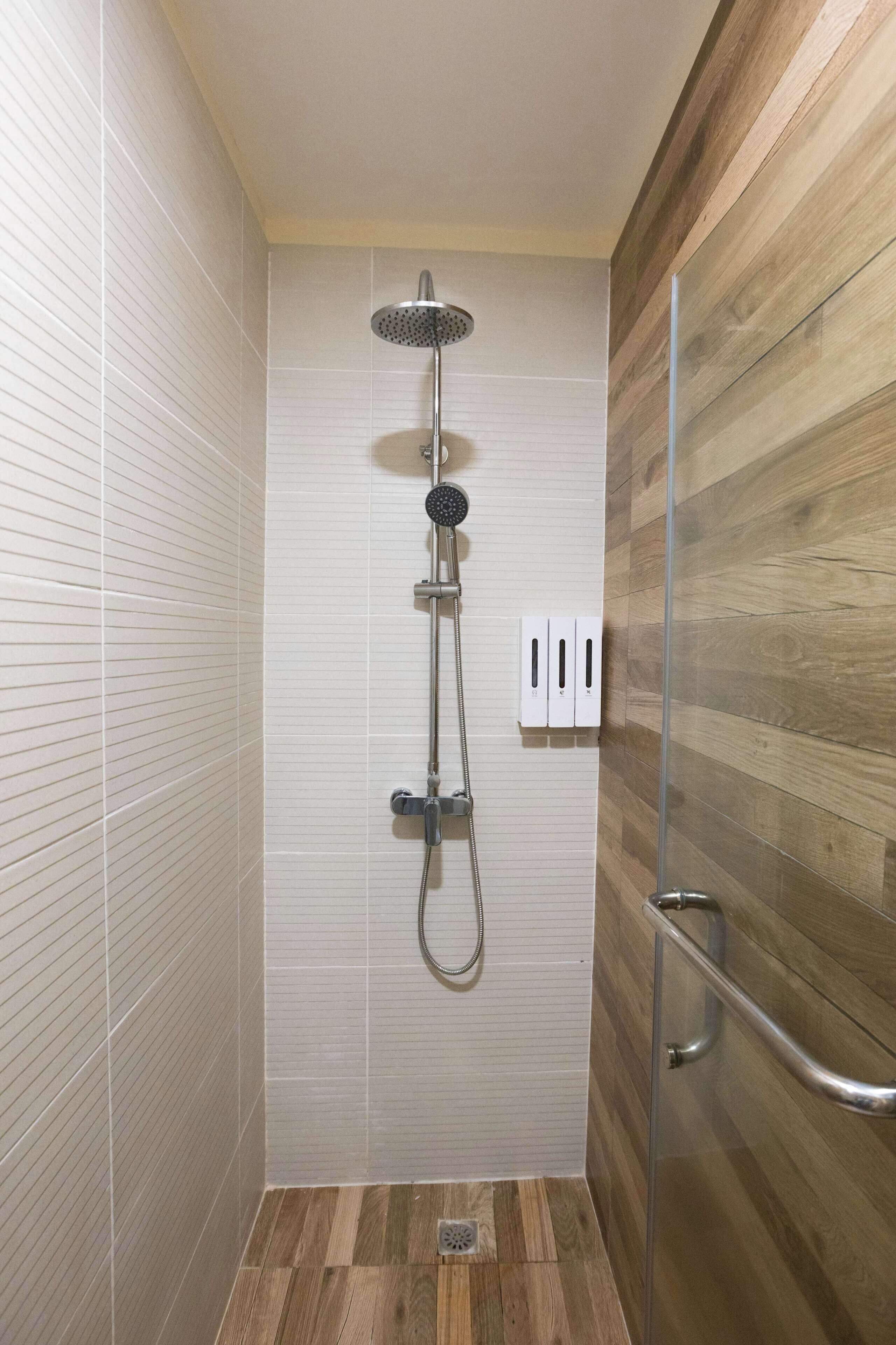 A shower with a handheld showerhead, a wall-mounted control panel, and a wooden floor.