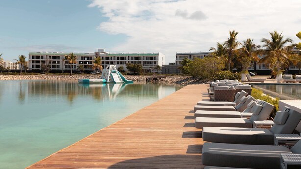 Ein Hotelpool mit Liegestühlen, einer Holzterrasse und einem Gebäude im Hintergrund.