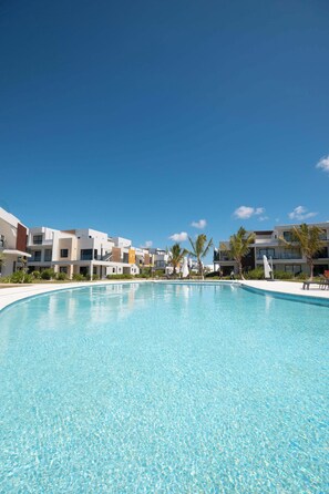 A clear blue swimming pool surrounded by modern buildings with balconies, under a clear sky. - NOK Cozy 2BR Stay in Vistacana Punta Cana (Punta Cana)