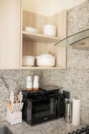 Uma cozinha com micro-ondas, porta-facas, chaleira e um rolo de papel toalha.