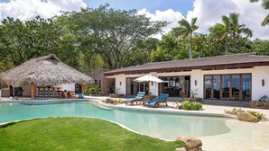 A pool area with lounge chairs, a thatched-roof structure, and a modern building with large windows. - Beautiful luxury house in Guacalito de la Isla, Casa Kidd (Tola)