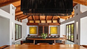 A dining area with a wooden table and chairs, a hanging light fixture, and large windows. - Beautiful luxury house in Guacalito de la Isla, Casa Kidd (Tola)