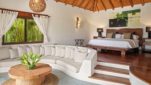 A modern bedroom with a curved sofa, a bed with a wooden headboard, a ceiling fan, and a large window with curtains. - Beautiful luxury house in Guacalito de la Isla, Casa Kidd (Tola)