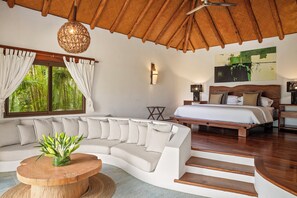Ein modernes Schlafzimmer mit einer gebogenen Couch, einem Bett mit Holz Kopfteil, einem Deckenventilator und einem großen Fenster mit Vorhängen.