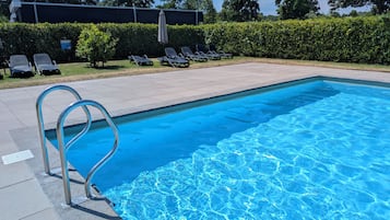 Una piscina azul cristalina con una escalera metálica, rodeada de una terraza pavimentada y sillas de descanso.