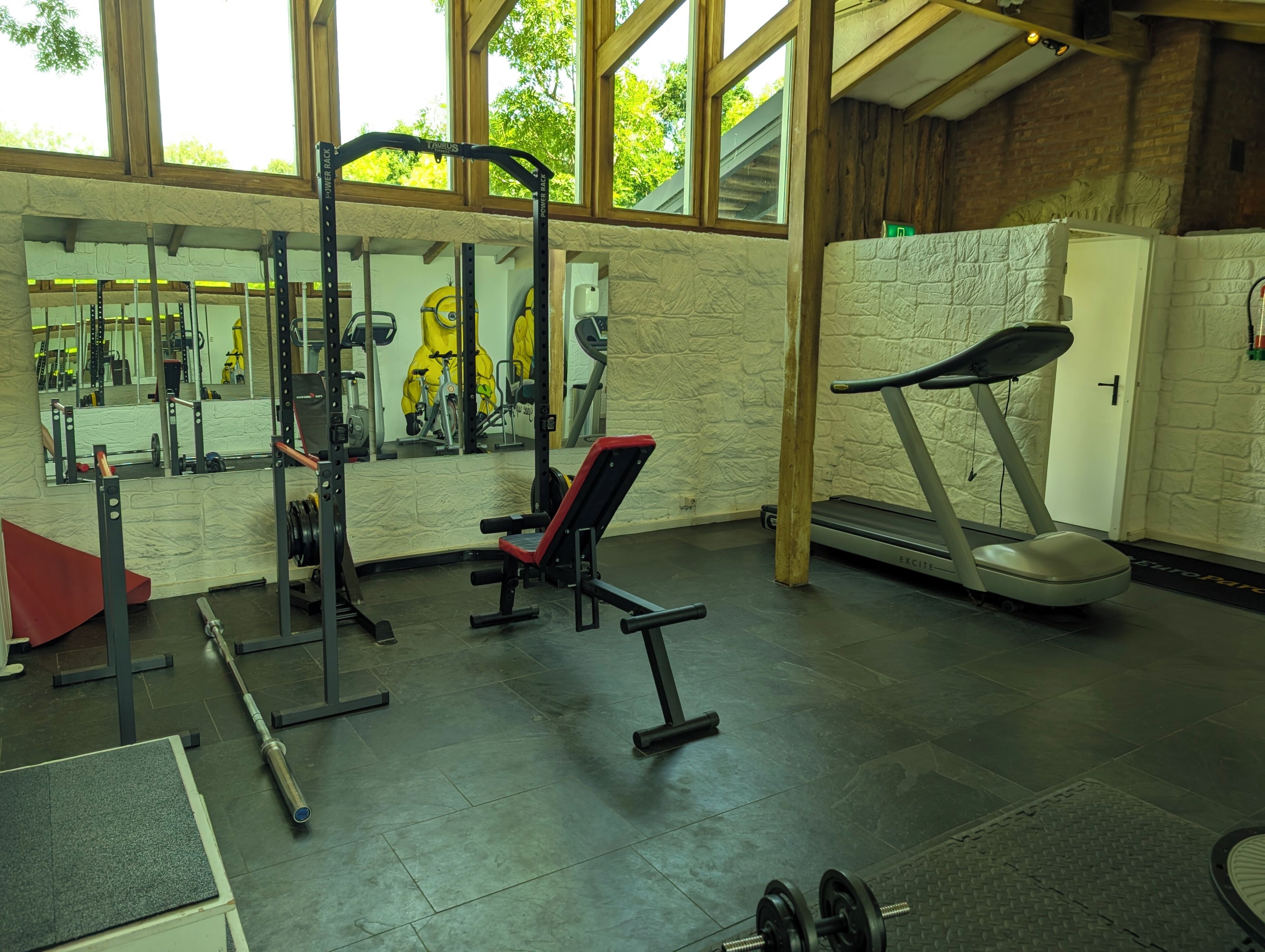 Uma academia com equipamentos de exercícios, um espelho e uma esteira.