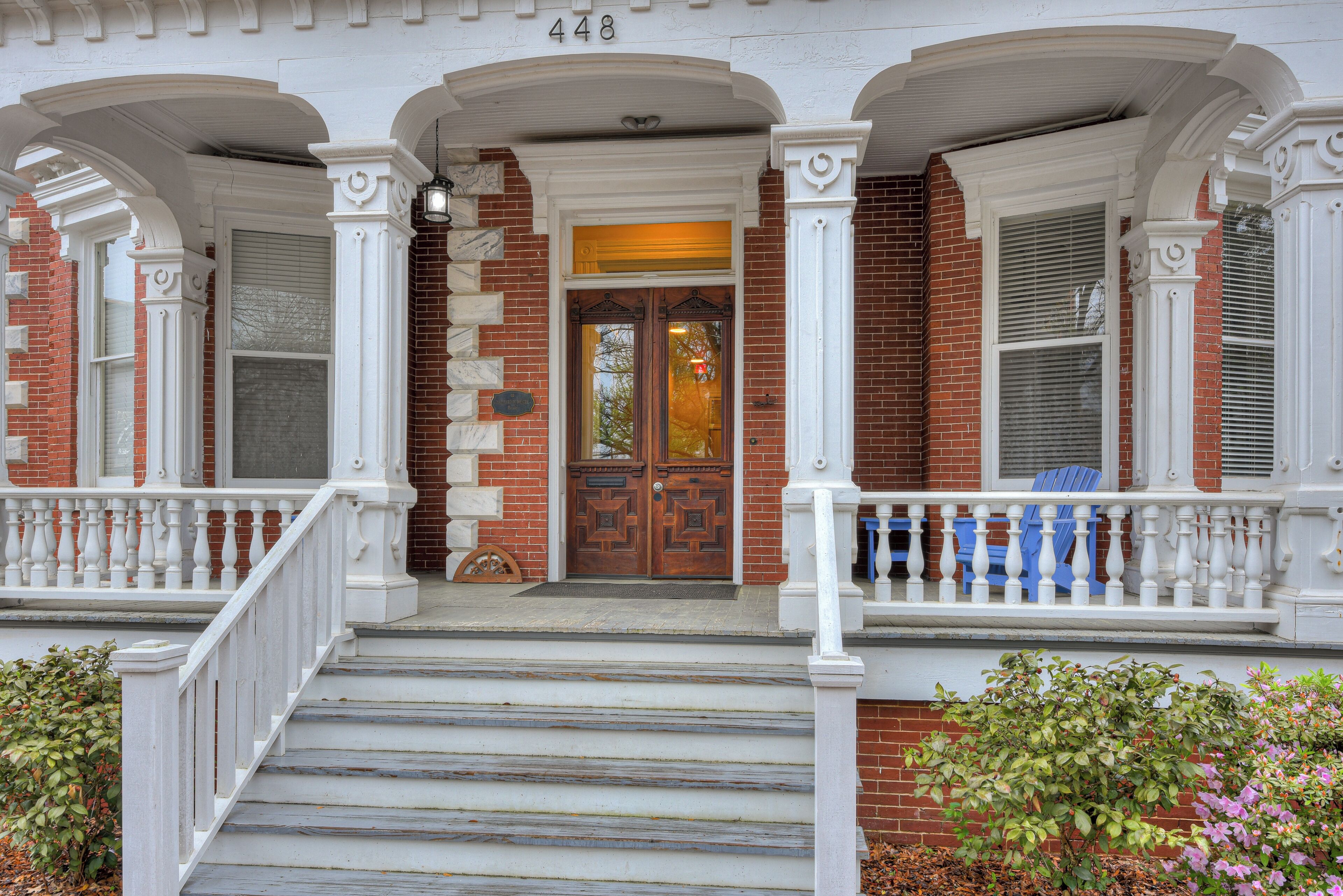 A two-story house with a front porch, a brick facade, and a double door.