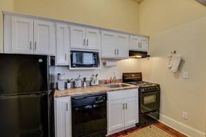 Una cucina con mobili bianchi, un frigorifero nero, un forno a microonde, un piano cottura e una lavastoviglie.