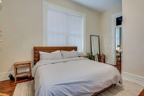 Un dormitorio con cama, mesita de noche, espejo y ventana con persianas.