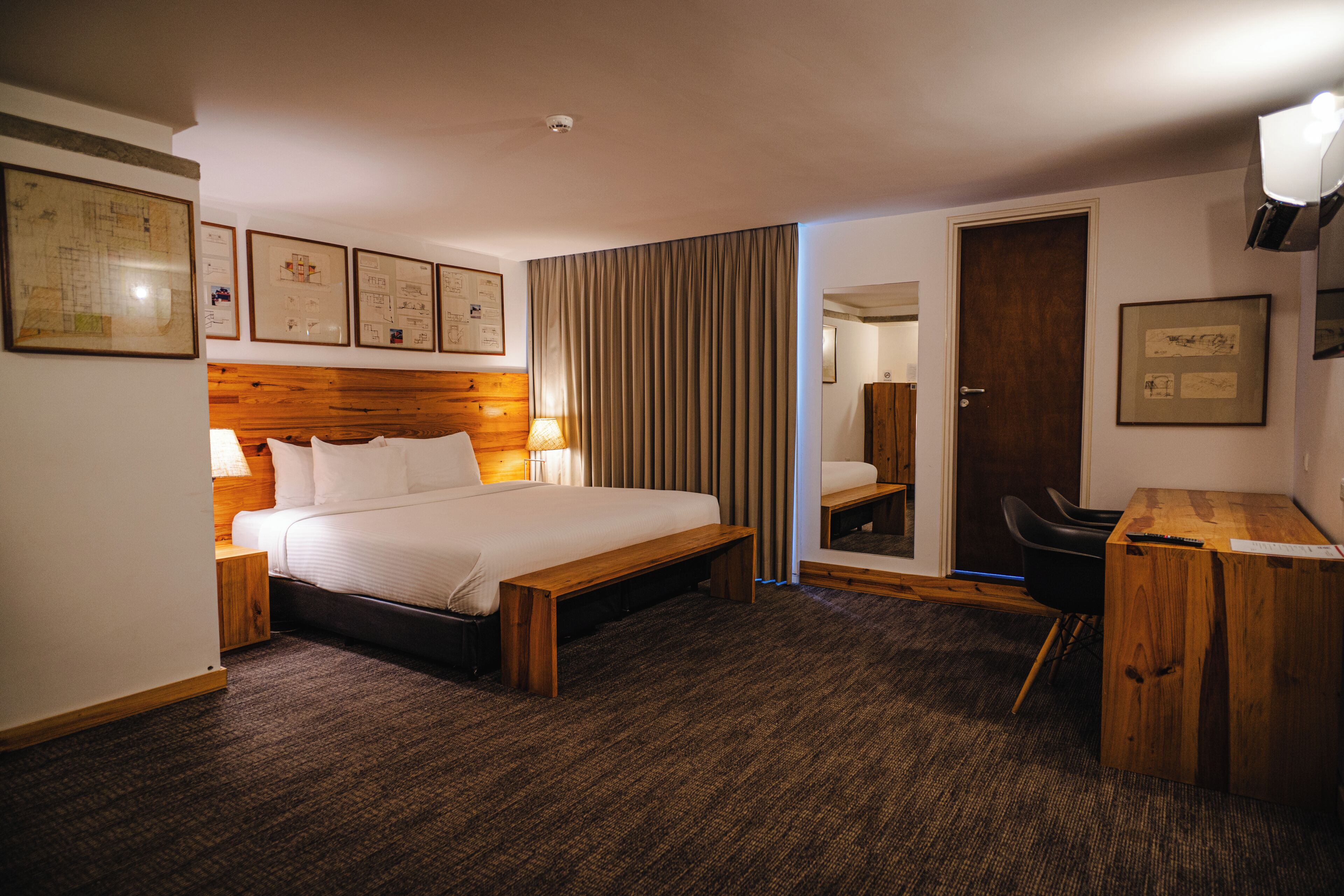 Ein Hotelzimmer mit Bett, Nachttisch, Lampe und Schreibtisch mit Stuhl.