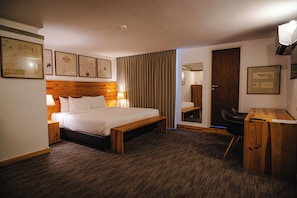 Una habitación de hotel con cama, mesita de noche, lámpara y un escritorio con silla.