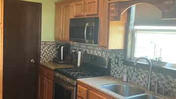 A kitchen with wooden cabinets, a stainless steel sink, a microwave, a stove, and a window with a view.