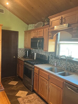 A kitchen with wooden cabinets, a stainless steel sink, a microwave, a stove, and a window with a view.