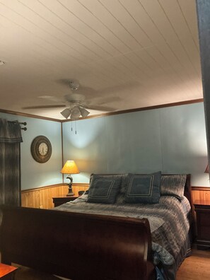 A bedroom with a bed, a nightstand, a lamp, a ceiling fan, and a wall clock.