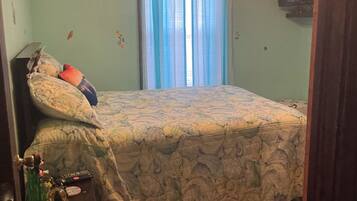 Une chambre à coucher avec un lit, un ventilateur de plafond, une fenêtre avec des rideaux et un téléviseur fixé au mur.