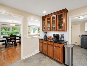 A kitchen with wooden cabinets, a black countertop, and a stainless steel trash can. - Casa Newburg | Hot Tub • Game Garage • Fenced Yard (Louisville)