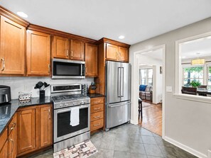 A modern kitchen with wooden cabinets, stainless steel appliances, and a tiled floor. - Casa Newburg | Hot Tub • Game Garage • Fenced Yard (Louisville)