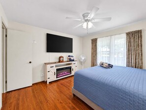 A bedroom with a bed, a television mounted on the wall, a ceiling fan, and a window with curtains. - Casa Newburg | Hot Tub • Game Garage • Fenced Yard (Louisville)