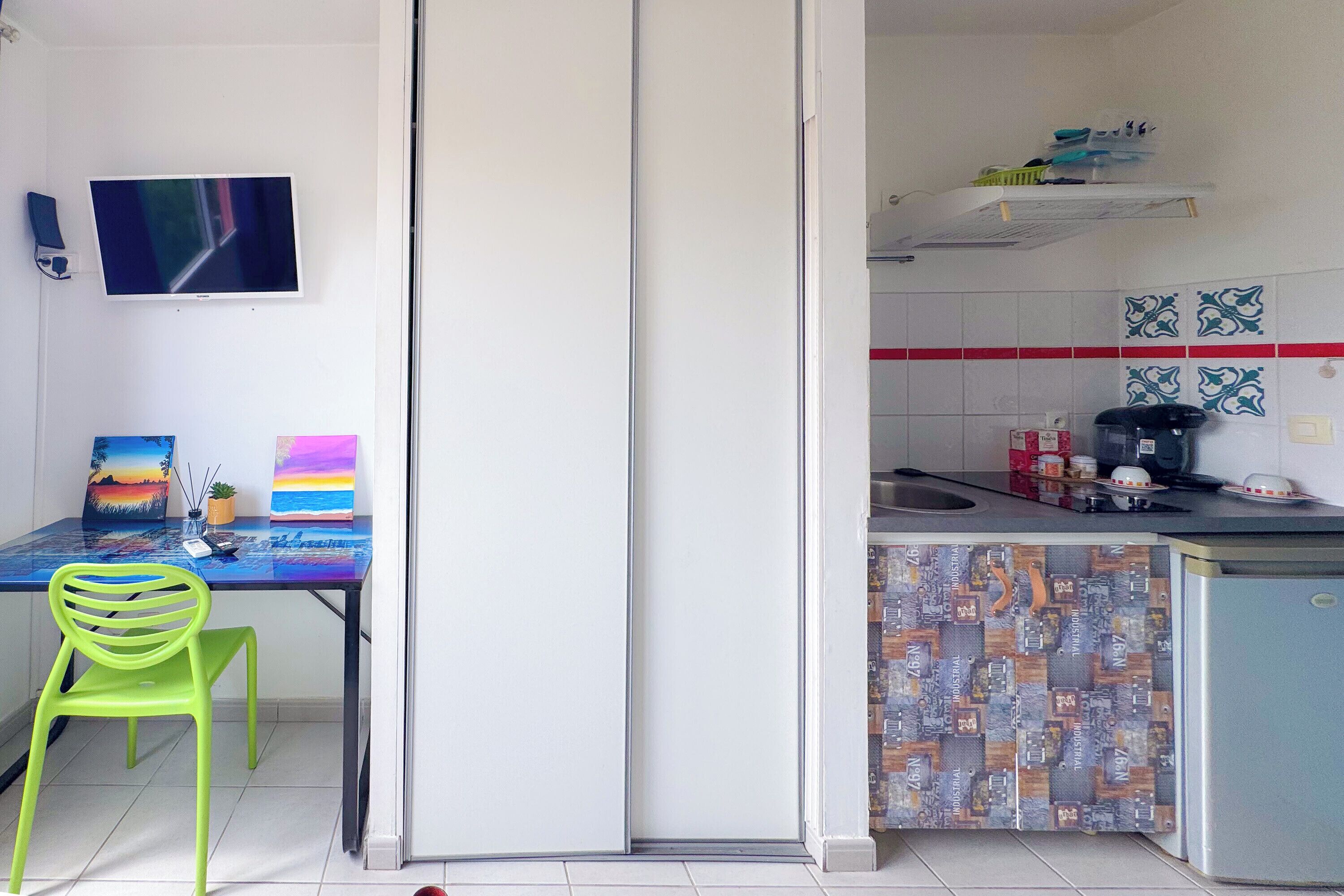 Ein Zimmer mit Essbereich, inklusive Tisch, Stühlen und Kunstwerken. Ein Küchenbereich ist erkennbar mit Spüle, Herd und gefliestem Rücksprung.