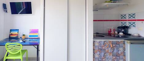 Ein Zimmer mit Essbereich, inklusive Tisch, Stühlen und Kunstwerken. Ein Küchenbereich ist erkennbar mit Spüle, Herd und gefliestem Rücksprung.