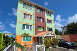 A multi-story building with a central red section and green and orange accents. - Le petit havre de paix - Climatisation (Schœlcher)