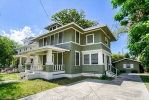 Ein zweistöckiges Haus mit Veranda, überdachter Auffahrt und kleinem Anbau für eine Garage.