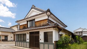 A traditional Japanese house with a tiled roof, wooden balcony, and a large sliding door.