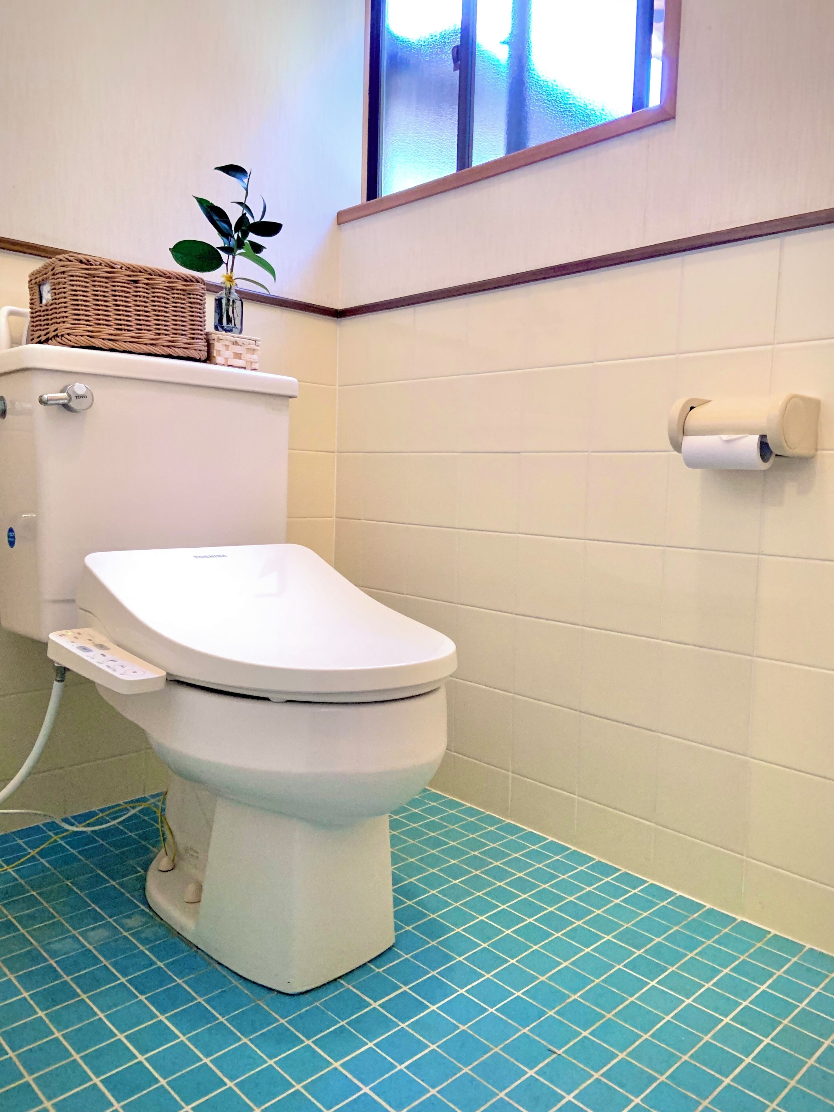 A toilet with a control panel, a roll of toilet paper on the wall, and a blue-tiled floor.