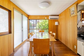 A wooden-paneled room with a dining table, chairs, a lamp, and an air conditioning unit.