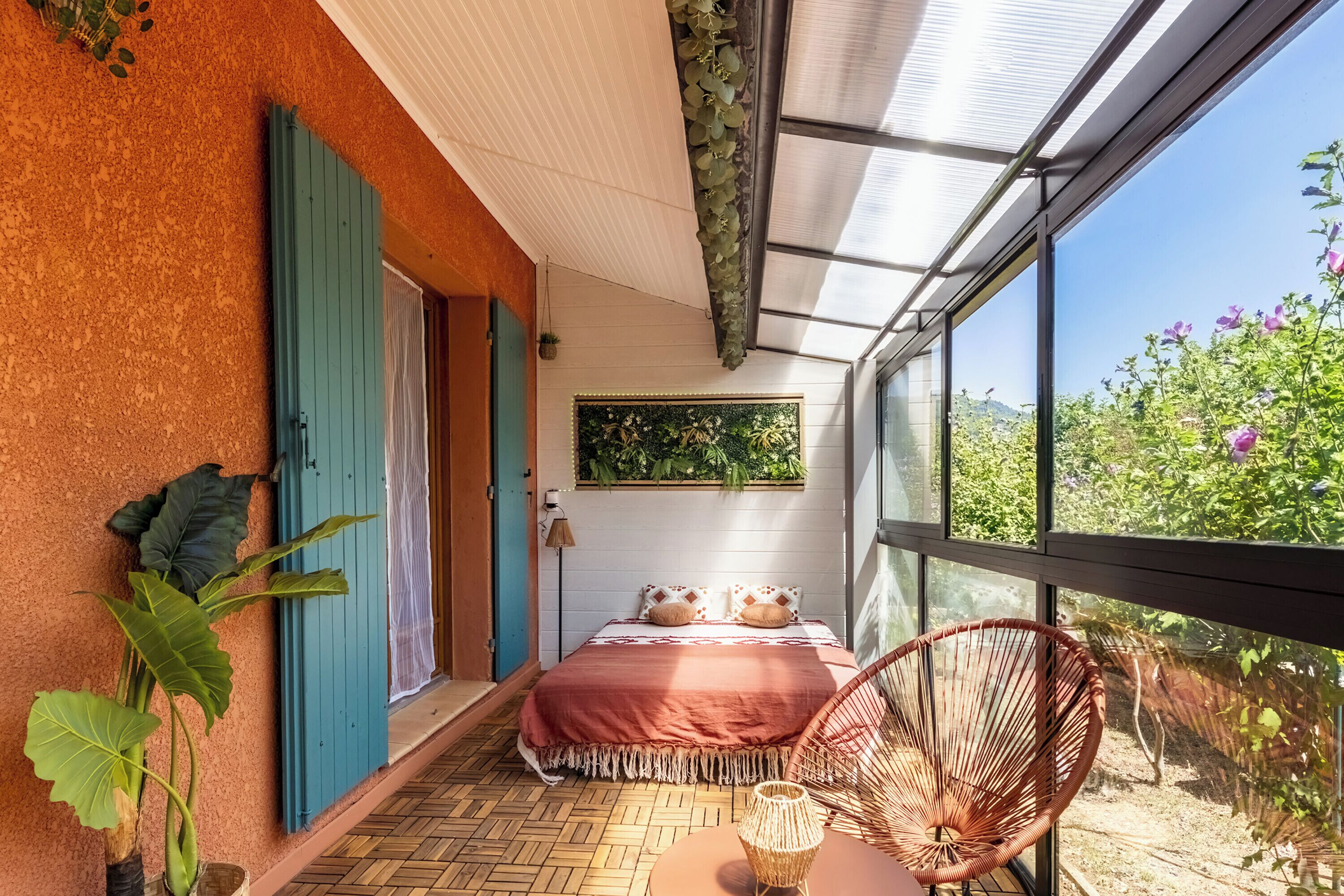 A room with a bed, a chair, a window, and a wall-mounted plant.
