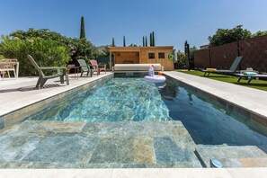 Piscina com água cristalina, rodeada por espreguiçadeiras e um deck de madeira.