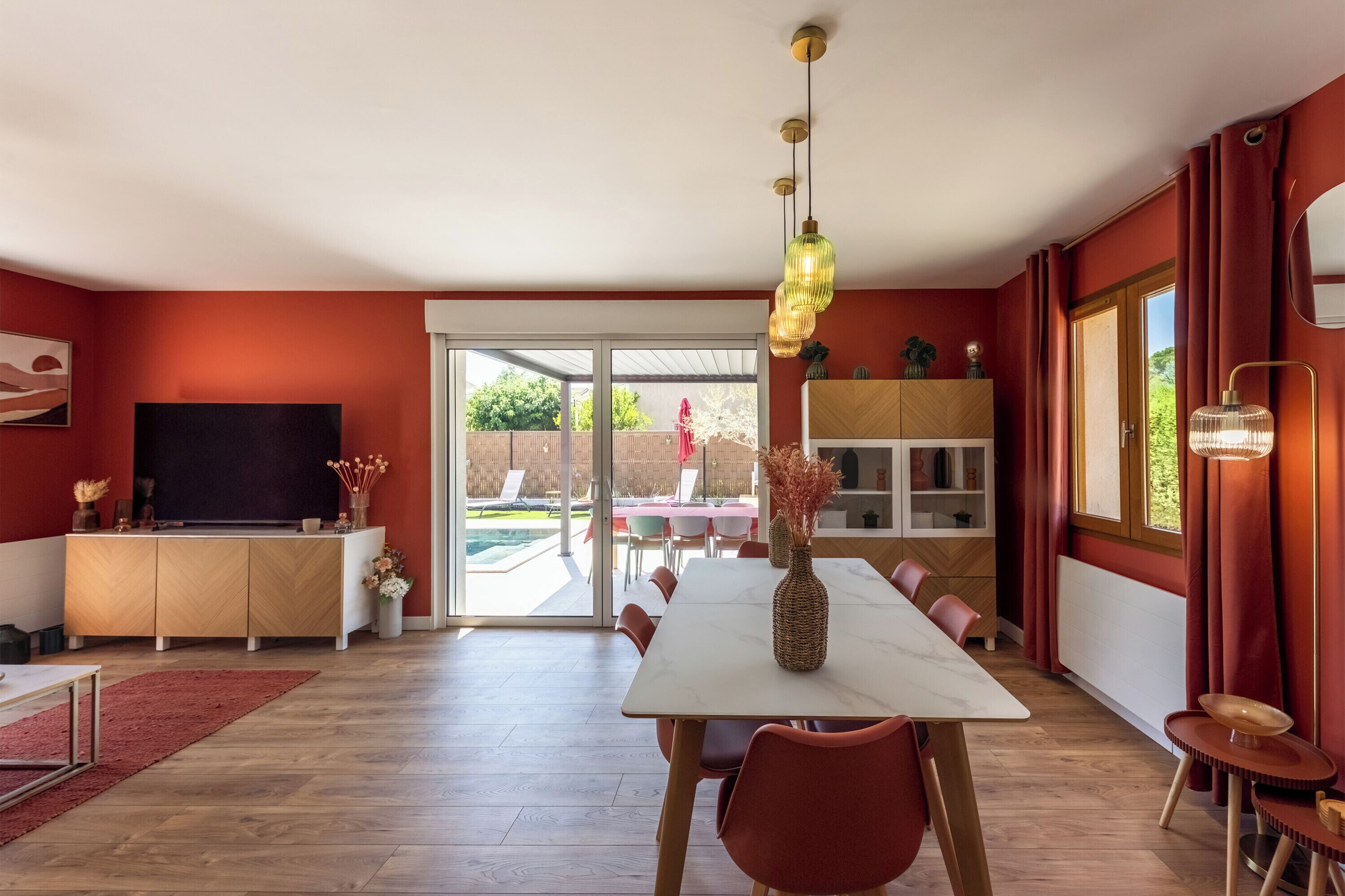 Ein moderner Essbereich mit einem großen Tisch, roten Stühlen und einem Fernseher auf einem Schrank.