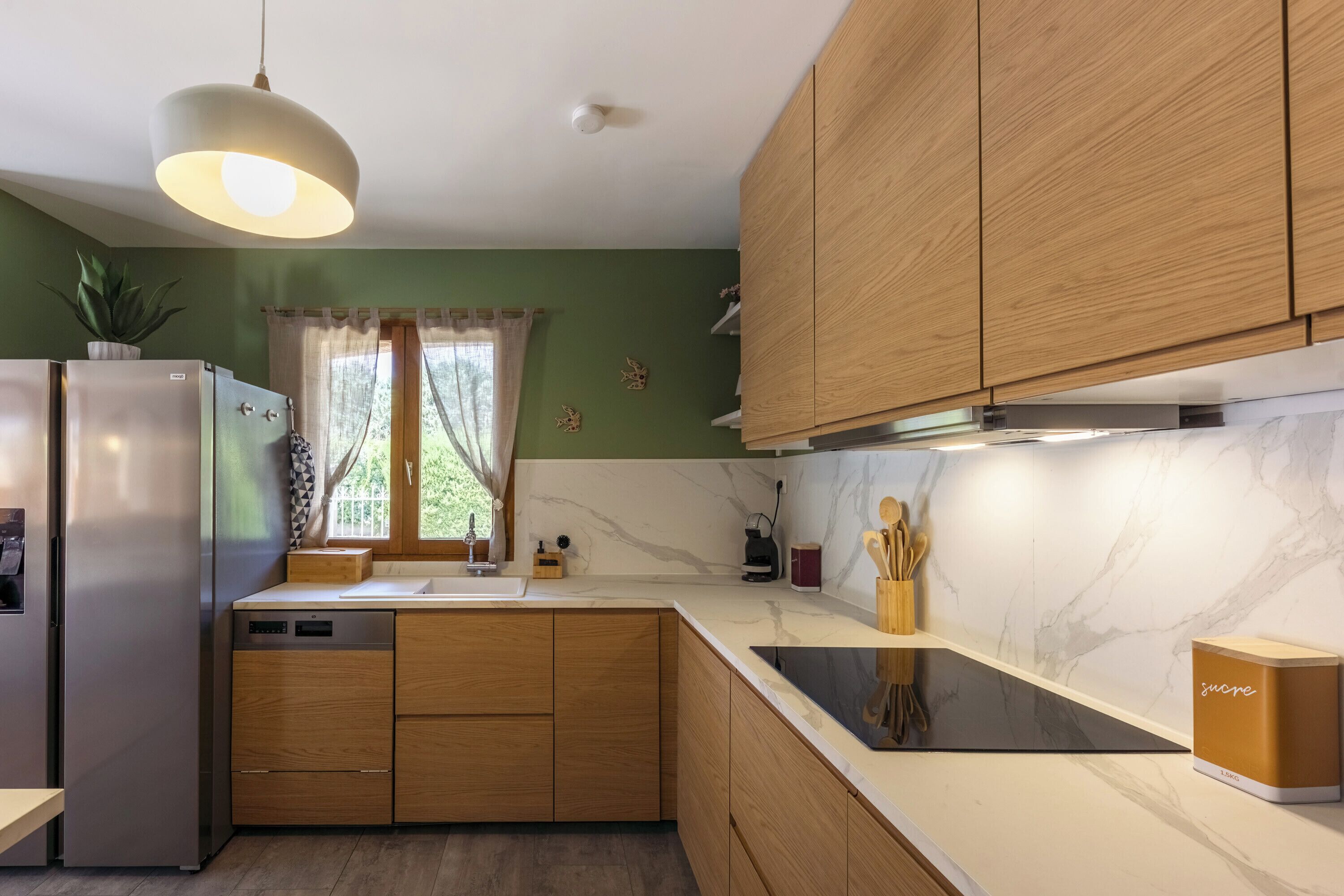 Une cuisine moderne avec des meubles en bois, un réfrigérateur en acier inoxydable, un plan de travail en marbre et un luminaire suspendu.