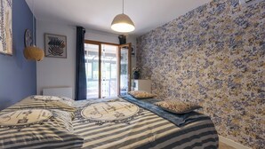 Un dormitori amb un llit, una làmpada penjant, una finestra amb cortines i una paret amb un disseny floral.
