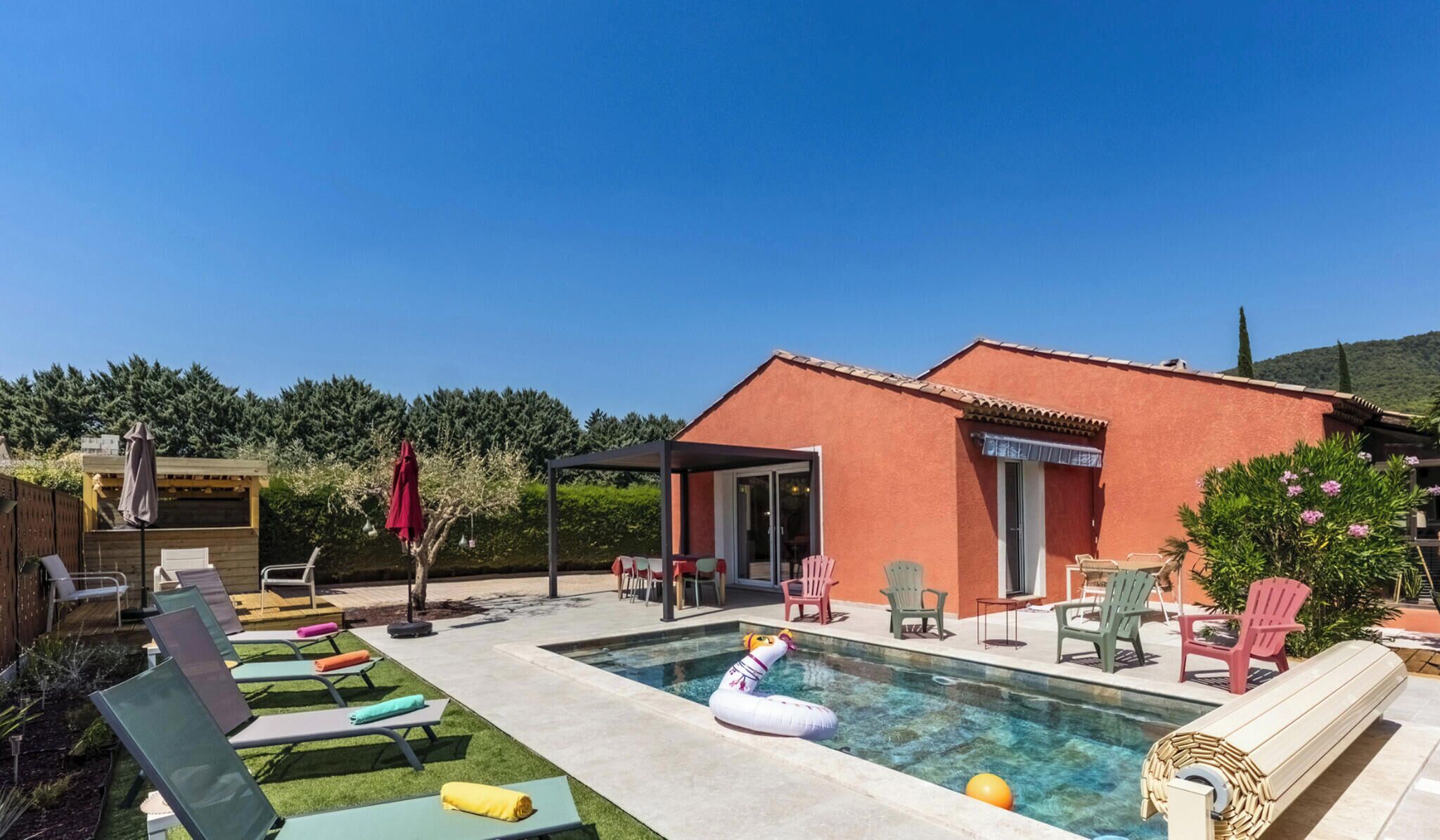 A pool area with lounge chairs, a covered seating area, and a building with a red exterior.