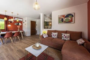 Ein modernes Wohnzimmer mit einem braunen Sofa, einem Essbereich mit roten Stühlen und einer Küche im Hintergrund.