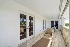 A covered outdoor balcony with a tiled floor, two doors, and a seating area with a table and chairs. - Luxury Oasis • Pool & Outdoor Kitchen • 12 Guests (Hialeah)