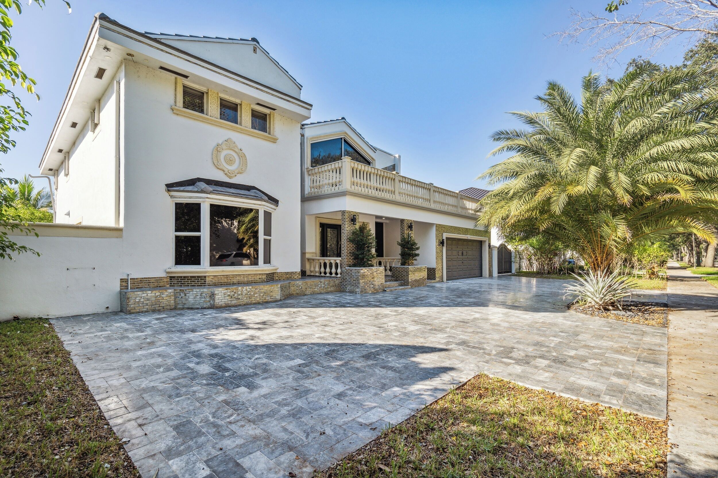 A two-story house with a paved driveway, a garage, and a landscaped garden with palm trees.