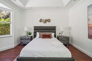 A bedroom with a large bed, two bedside tables, a headboard, and a window with a view of greenery. - Luxury Oasis • Pool & Outdoor Kitchen • 12 Guests (Hialeah)