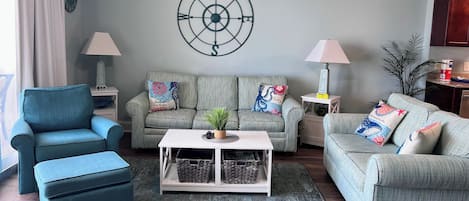 A living room with a blue armchair, two grey sofas, a coffee table, and a wall clock.