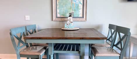Una mesa de comedor con cuatro sillas, un cuadro enmarcado encima y un pequeño objeto decorativo sobre la mesa.