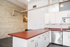 A modern kitchen with white cabinets, a wooden countertop, and a brick wall. - Spacious Exchange District Condo | 1 Bed | 1 Bath | (Winnipeg)
