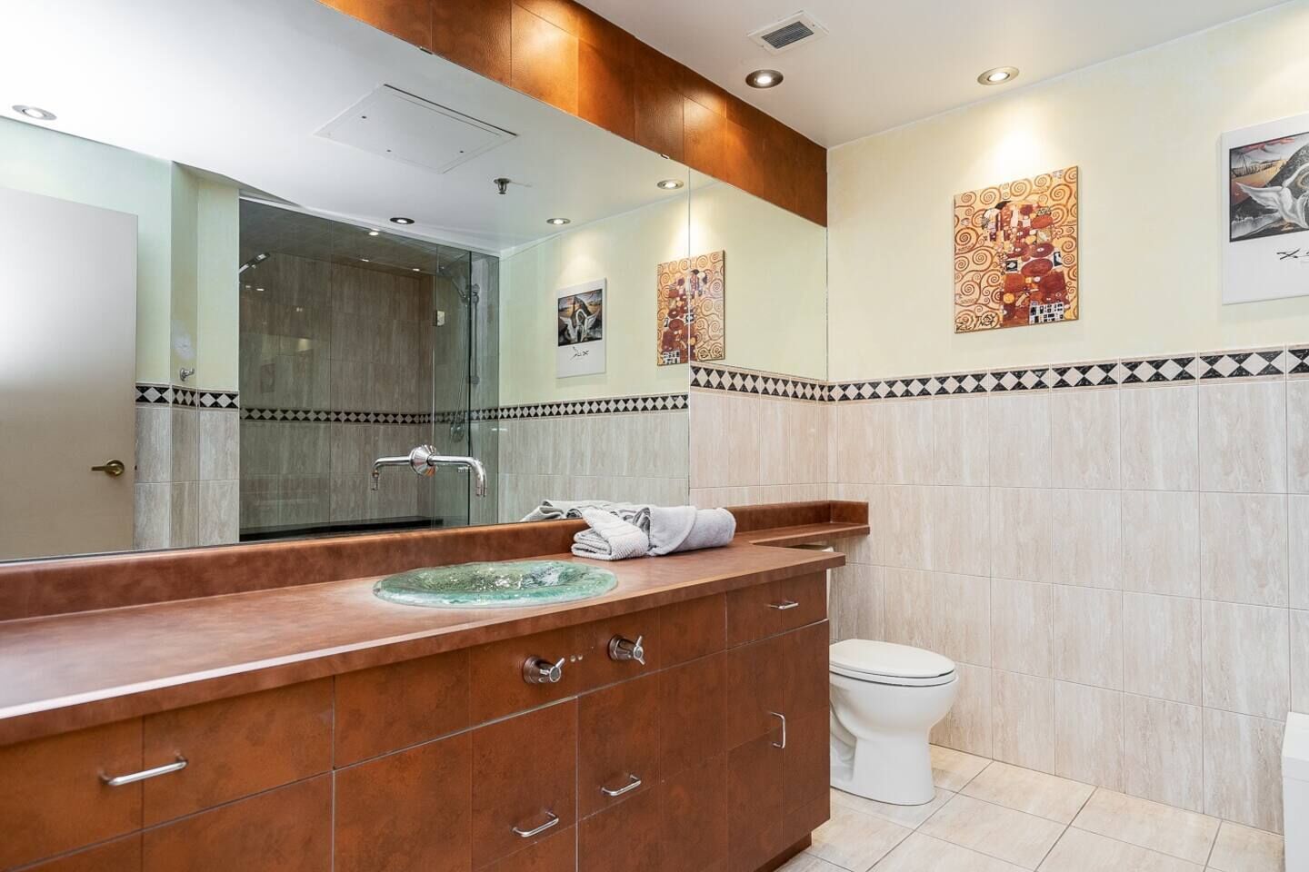 Un baño con cabina de ducha de vidrio, tocador de madera con lavamanos y un inodoro.